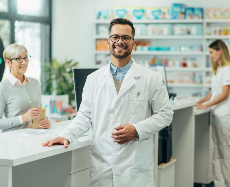 Pharmacist at the counter using a Pharmacy POS system to assist a customer in a modern pharmacy.